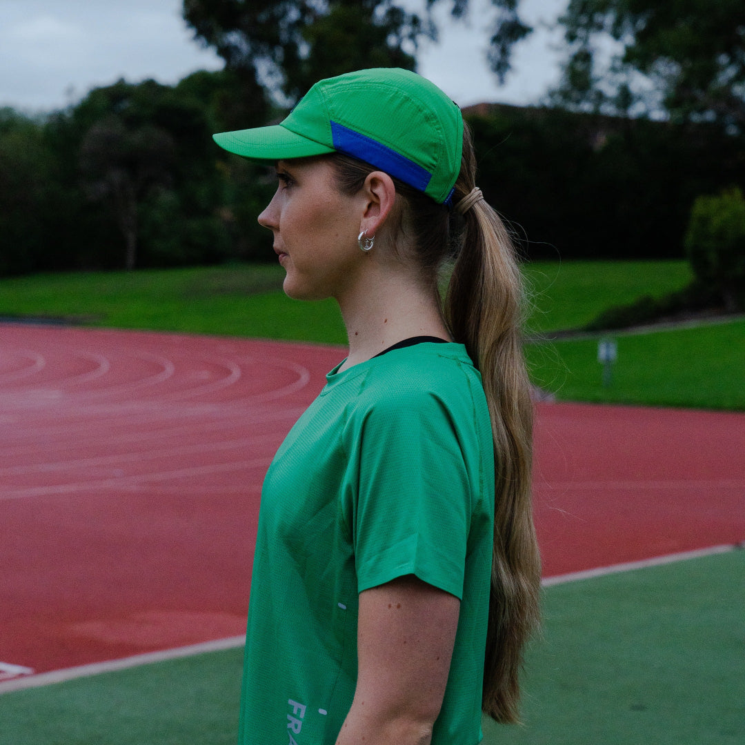Woman wearing a green cap and shirt on a track field